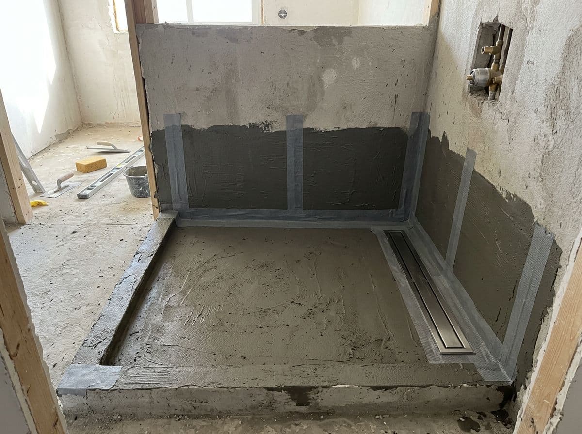 Pendiente e impermeabilización de la base de una ducha de obra con banda de refuerzo en los encuentros